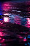 Water on a street at night reflecting pink light