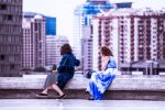 Two women sitting on a rooftop overlooking a city