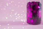 Glass bottle with purple heart shaped sparkles on pink background
